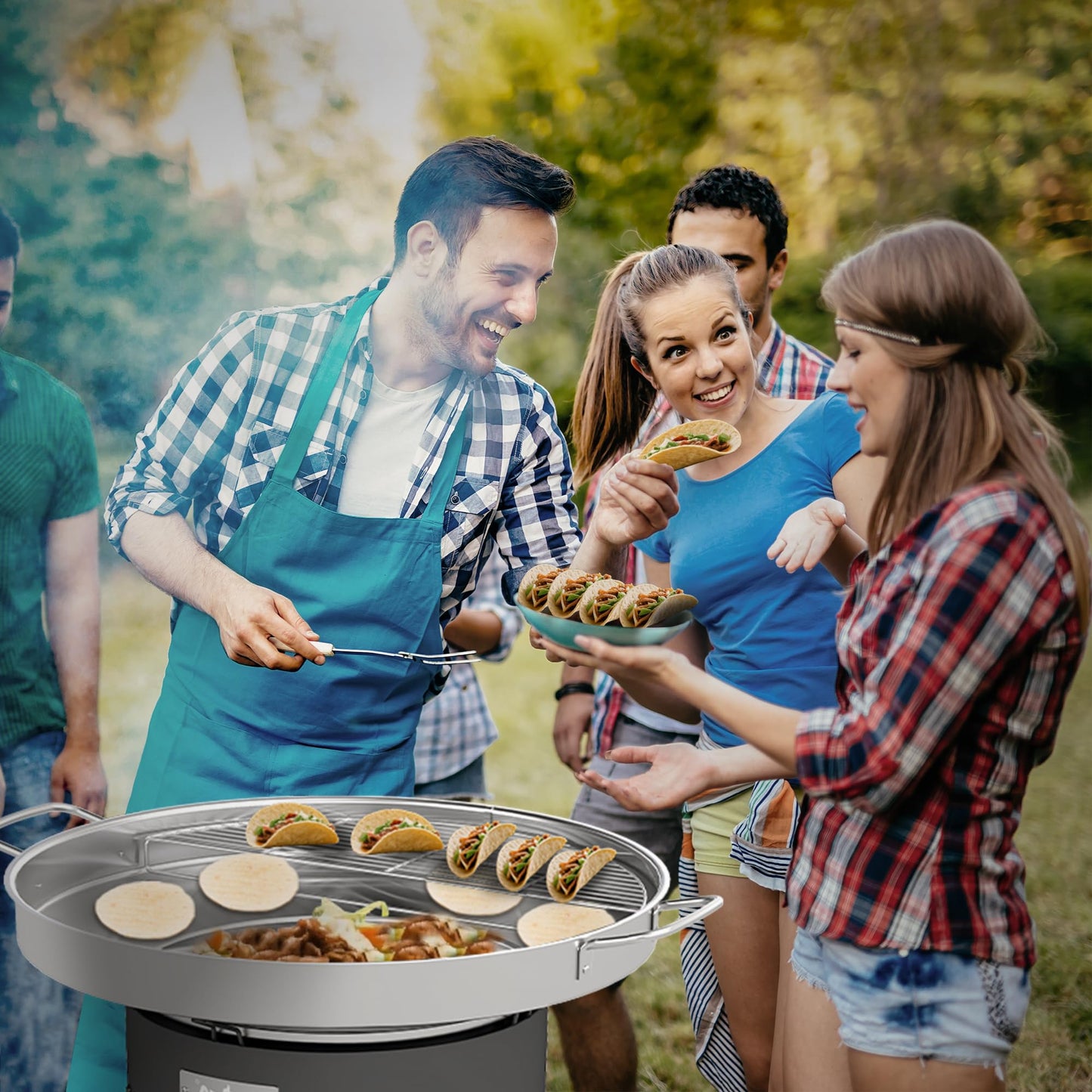 Group of people enjoying a barbecue outdoors with food and grilling equipment.